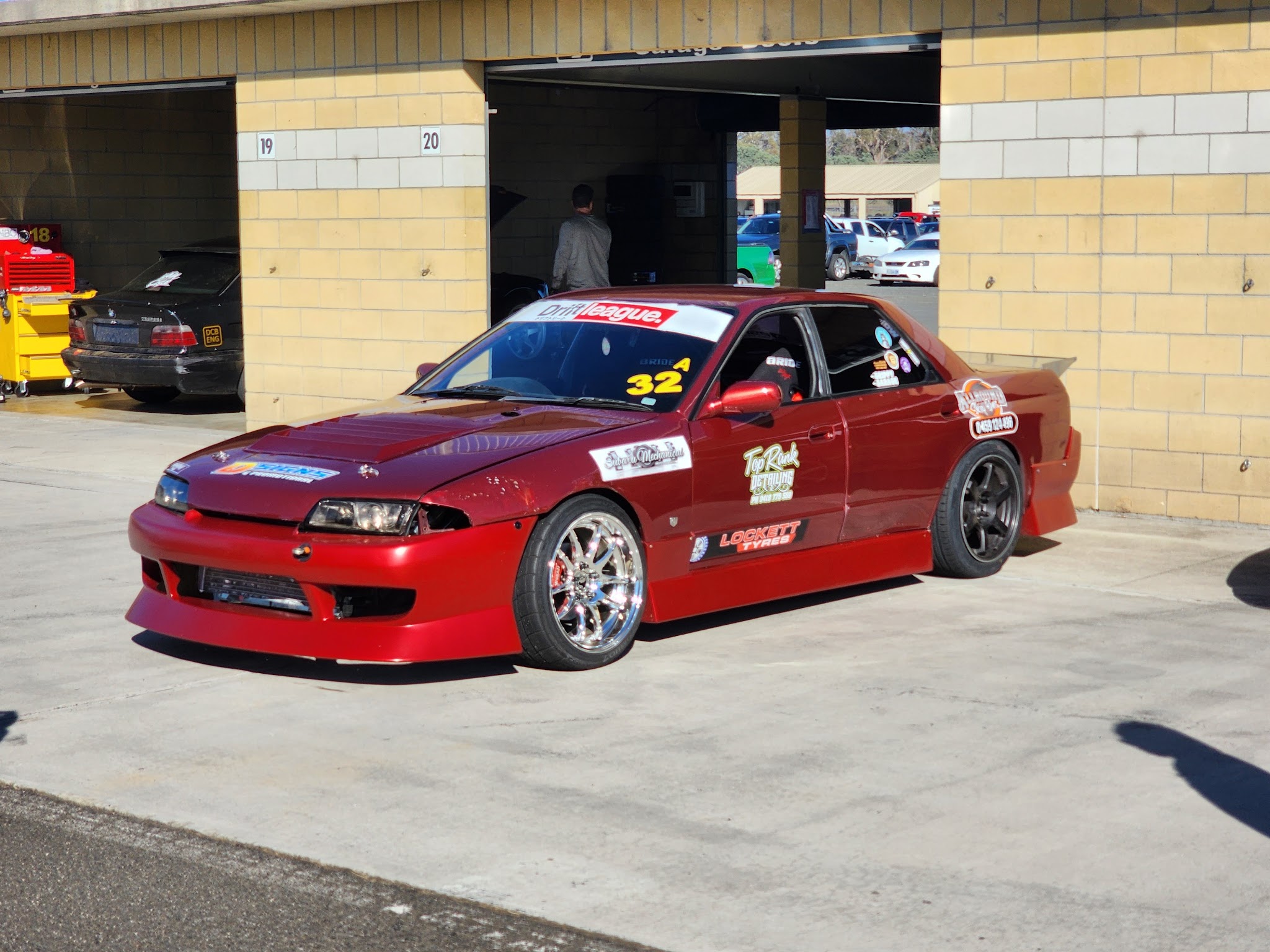 The red Nissan Skyline drift car carrying a Subaru Mechanical decal, in a circuit pit garage